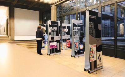 Exhibition installation featuring vertically arranged typographic banners presenting archival imagery and political research in a public interior space.