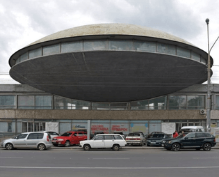 saucer-like-structure-with-windows-going-around-its-middle-attached-to-an-old-two-storey-building-with-multiple-windows-conc...