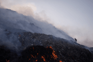 A waste collector looking for recyclable materials as smoke billows from burning garbage at the Bhalswa landfill site in New Delhi on Wednesday. Adnan Abidi / Reuters