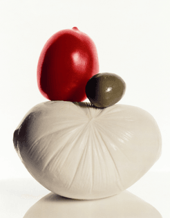 still life photograph of mozzarella, tomato, and olive, against a white background.