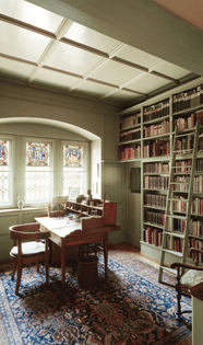 Carl Jung's office includes a wooden next next to stained glass windows. While seated at the desk, you see a wall of books with a ladder to reach the books on the higher shelves.
