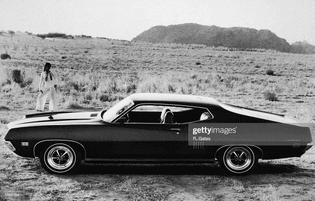 female-model-standing-behind-a-ford-gt-torino-in-a-desert-setting-picture-id1585754