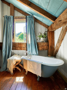 a-pretty-barn-bathroom-with-wooden-plank-walls-a-floor-and-ceiling-wooden-beams-a-blue-clawfoot-tub-and-blue-curtains-on-the...