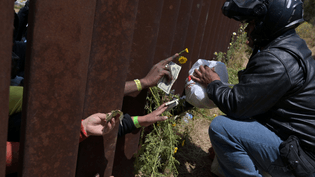 Migrants stuck at a border wall separating Tijuana and San Diego pay and collect food from a delivery person on May 11, 2023. Carlos Moreno