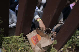 A migrant pulls a Burger King order from Uber Eats through a border wall on May 11, 2023. Carlos Moreno