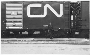 Fleming poses with his logo during a test application on a boxcar outside Toronto’s Union Station (1962; MF). Photographer: Kryn Taconis. Fleming was commissioned in 1959 to create the central logo of a huge corporate redesign for Canadian National Railways, then government-owned.