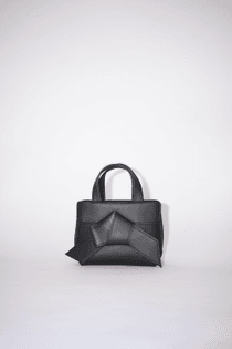 Acne Studios black micro tote bag is made of soft leather and is adorned with a twisted musubi knot on the front, inspired by traditional Japanese obi sashes. Completed with a middle zippered pocket compartment and a discrete zippered closure.
