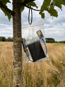 a computer and solar panel hanging in a clear plastic bag in a tree